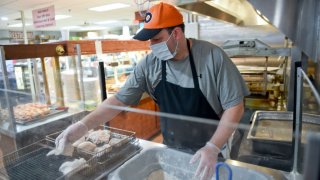 A man wearing a Flyers hat and face mask breads chicken at a restaurant.