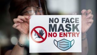 A woman puts a sign saying “no face mask no entry” in a shop window