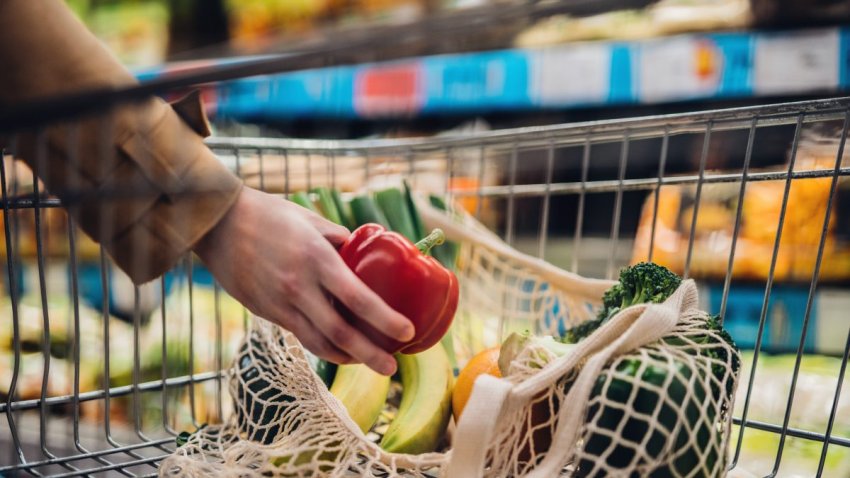 Close-up shot of female hand putting a red bell pepper into a mesh grocery bag. Shopping with eco-friendly shopping bag for a sustainable lifestyle.