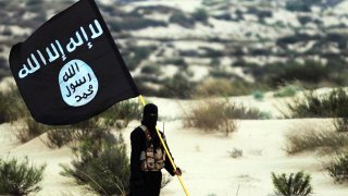 Un miliciano de ISIS posa con la bandera del grupo terrorista, en el desierto en Irak.