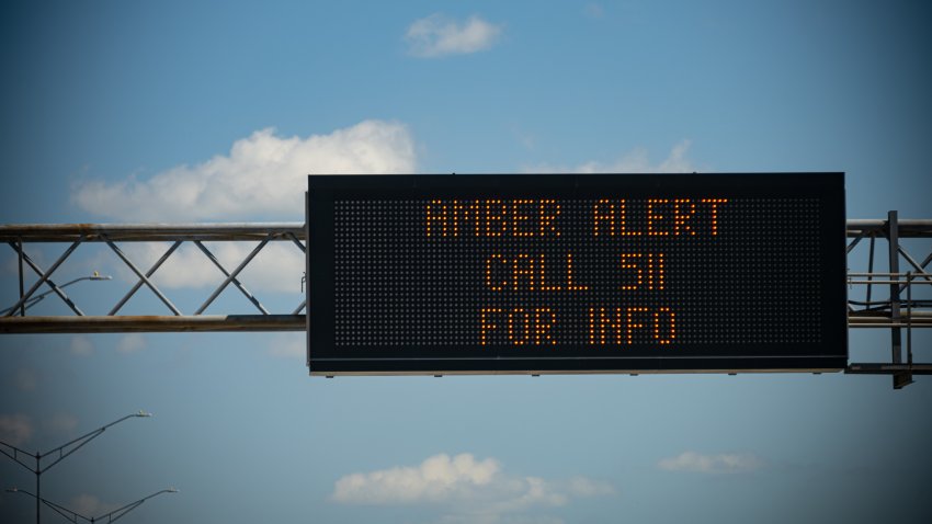 A digital sign above a busy highway alerts drivers to a current Amber Alert.