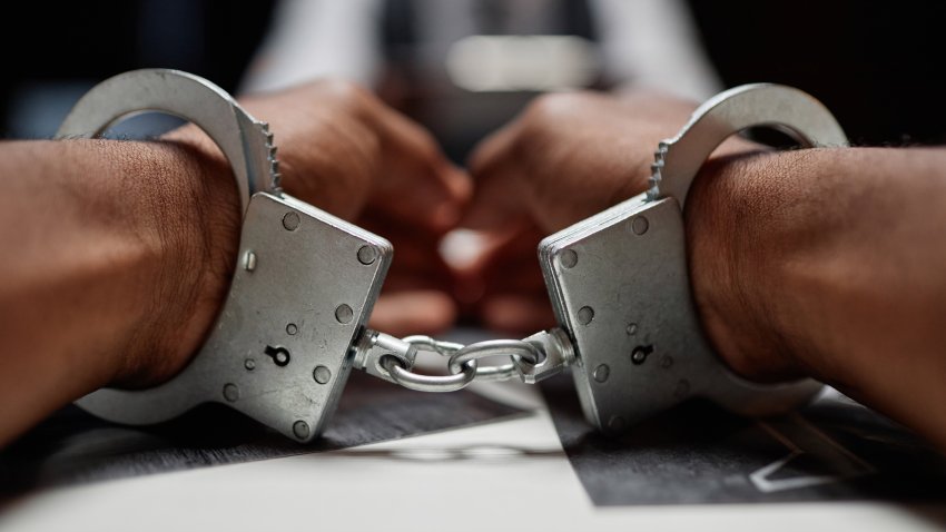 Dramatic close up of Black man wearing handcuffs on hands, criminal suspect
