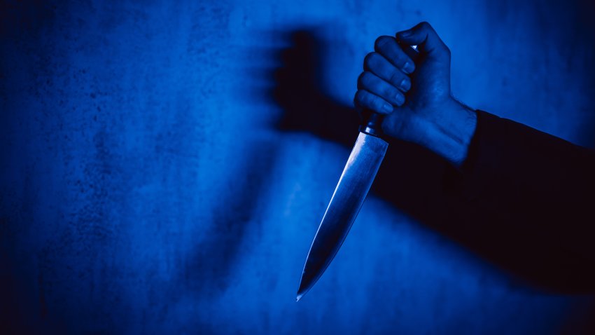 Close-up of a man holding a knife under neon lights.