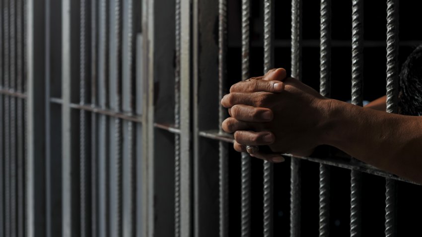 prisoner’s hands behind bars with black background