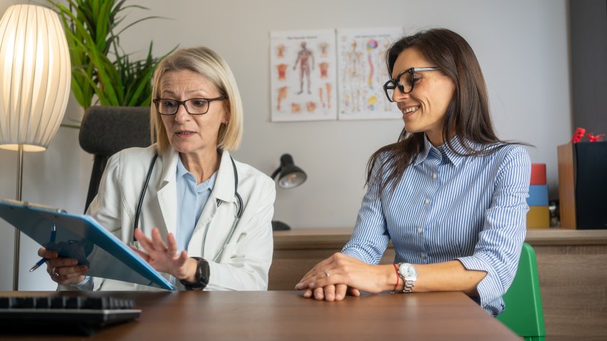Smiling female doctor with clipboard talking with middle aged female patient in doctor office. Doctor questioning patient and writing answers in clipboard. medicine, healthcare and people concept