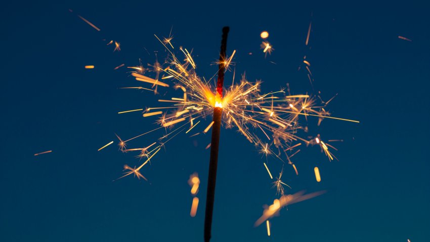 A fiery sparkler throws sparks in front of a dusk sky.  Photo taken on July 4 2022 in Utah USA.